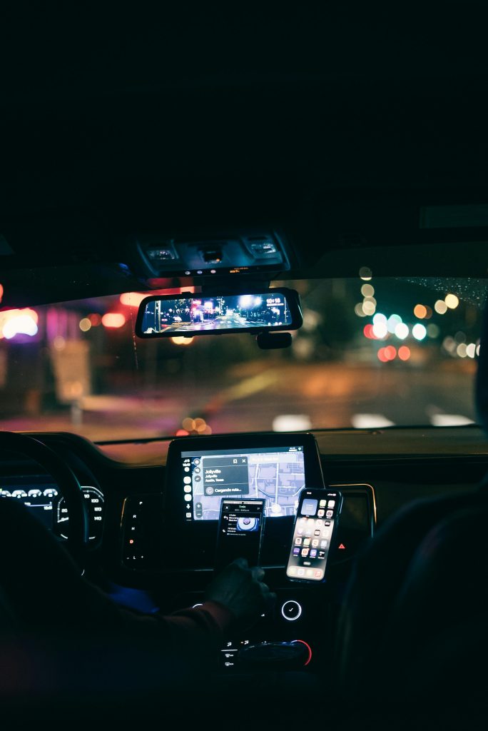 A car interior at night showing GPS navigation on a smartphone with city lights in the background.